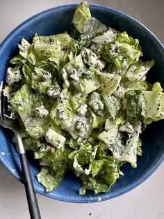 a blue bowl filled with lettuce and cheese on top of a white table