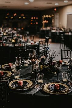 the table is set up for an event with black linens and gold place settings