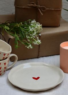 two cups and a plate with hearts painted on them sitting next to some wrapped presents