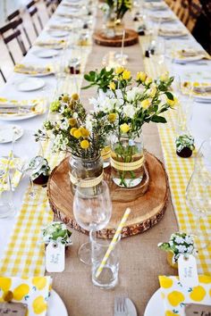 the table is set with yellow and white flowers in mason jar vases on wood slices