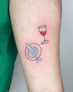 a person with a tattoo on their arm holding a wine glass and fish in it