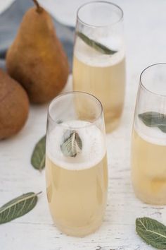 three glasses filled with liquid next to pears