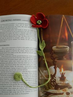 an open book with a crocheted flower on it and a candle in the background