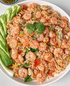 a white plate topped with rice and shrimp next to a bowl of vegetables on a table