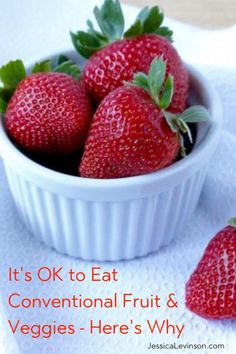 some strawberries are in a white bowl on a towel with the words it's ok to eat conventional fruit & veggies - here's why