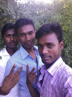 three men standing next to each other in front of some bushes and trees with one pointing at the camera