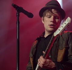 a man with a hat playing an electric guitar in front of a microphone on stage