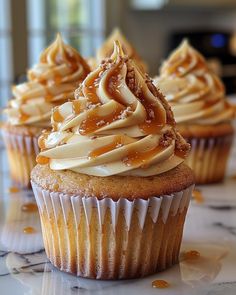 three cupcakes with frosting and caramel toppings on a marble table