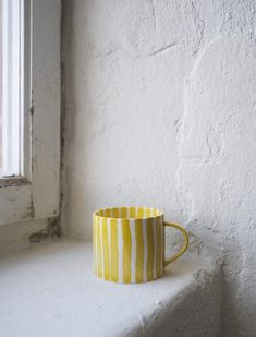 a yellow and white cup sitting on top of a window sill