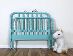 a white stuffed unicorn sitting next to a blue crib with the word new color written on it