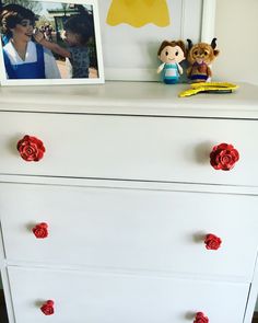 a white dresser with red knobs and flowers on the bottom drawer next to a framed photo