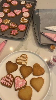 some heart shaped cookies are on a white plate next to a baking pan and pink utensils