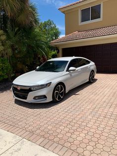 a white car parked in front of a house with a driveway and palm trees behind it