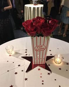 red roses in a popcorn box centerpiece on a white table with candles and people standing around