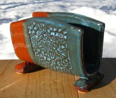 an orange and blue vase sitting on top of a wooden table next to snow covered ground