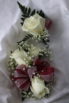 two white roses and baby's breath are arranged on a bed with red ribbon