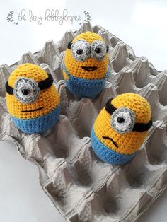 three crocheted yellow and blue minion balls in an egg carton on a white surface