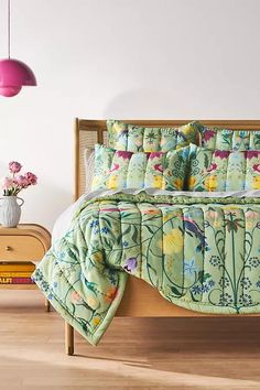 a bed sitting in a bedroom next to a wooden headboard and table with flowers on it