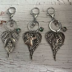 three key chains with angel charms hanging from them on a white wooden surface and one has a bird in the middle