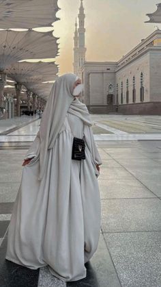 a woman in a long white dress standing on the sidewalk with an umbrella over her head