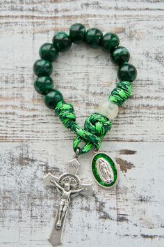 a green beaded bracelet with a silver cross on it and a medal hanging from the clasp