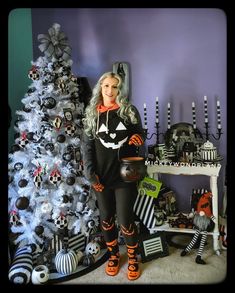 a woman standing next to a christmas tree in front of a purple wall with black and white decorations