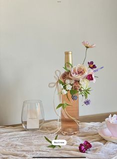 a table topped with a vase filled with flowers and a bottle of wine next to it