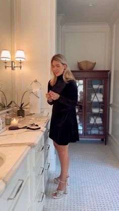 a woman standing in front of a bathroom sink next to a counter with candles on it