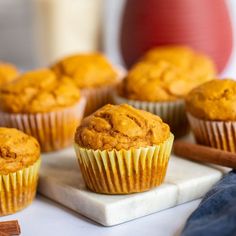 several muffins sitting on a white plate next to cinnamon sticks and an orange vase