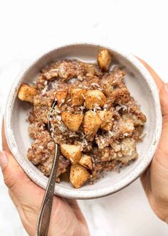 two hands holding a white bowl filled with oatmeal and cinnamon croutons