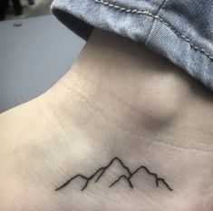 a small mountain tattoo on the side of a woman's neck is shown in black ink