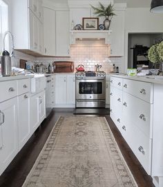 a kitchen with white cabinets and an area rug on the floor in front of the stove