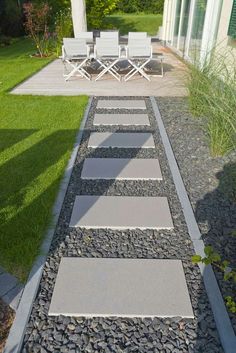 a walkway made out of stones leading to a patio with lawn chairs and table in the background