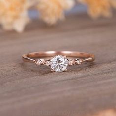 a rose gold engagement ring with a round brilliant diamond in the center, on top of a wooden surface