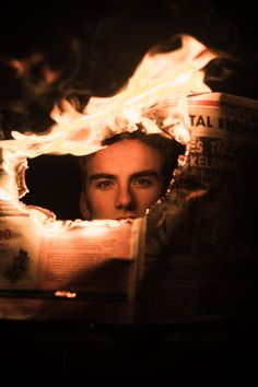 a man reading a newspaper with flames coming out of his face and the paper in front of him