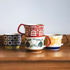 three colorful cups sitting on top of a wooden table