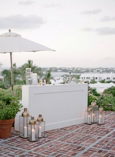 an outdoor bar is set up with candles and vases on the brick floor next to potted plants