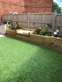 a wooden planter filled with lots of plants next to a brick wall and green grass