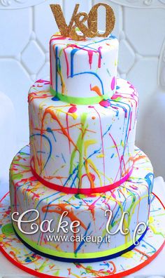 a three tiered cake with colorful icing and gold letters on top that says we do