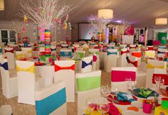 a room filled with tables and chairs covered in colorful napkins, place settings and centerpieces