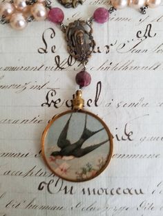 "The image of an antique (1900 - 1908) French Souvenir postcard (reproduced from my personal collection) in a vintage brass bezel.  The front is a swallow delivering a letter with the reverse image pink roses and the message, and can be worn with either side in front. The necklace measures 18\" of hand wire wrapped (sterling silver), vintage soft pink glass pearls, pink tourmaline disks, a brass reproduction Mary rosary connector, and a vintage brass rose holy medal.  the drop and pendant add an Vintage Gold Jewelry Souvenir, Antique Gold Necklace With Vintage Charm, Vintage Antique Finish Jewelry Gift, Vintage Antique Gold Jewelry Gift, Vintage Antique Finish Necklace For Gift, Vintage Jewelry With Antique Finish For Gift, Vintage Antique Finish Necklace As Gift, Vintage Jewelry With Antique Finish As Gift, Vintage Antique Gold Jewelry For Gift