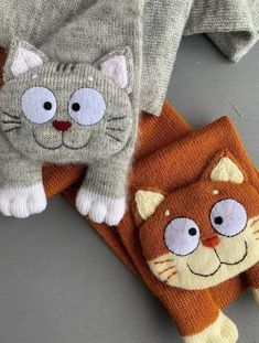 two knitted cat mittens laying on top of each other next to a sweater