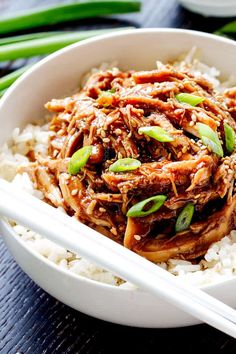 a white bowl filled with shredded meat and rice next to chopsticks on a table