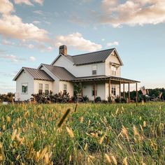 a large white house sitting on top of a lush green field next to tall grass