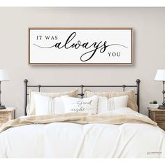 a bed with white sheets and pillows in front of a wall mounted sign that says it was always you