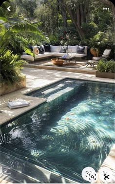 an outdoor swimming pool surrounded by greenery and furniture in the middle of a garden