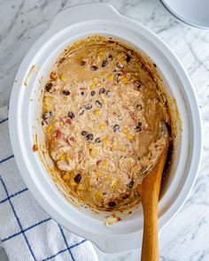 a white bowl filled with oatmeal and raisins next to a wooden spoon