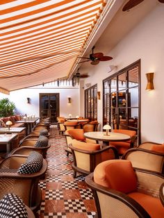 an outdoor restaurant with checkered flooring and orange cushions on the tables, along with ceiling fans