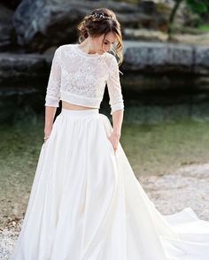 a woman in a white wedding dress standing next to a river with her hands on her hips