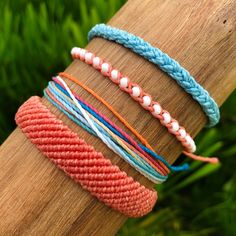 four different colored bracelets sitting on top of a wooden stick